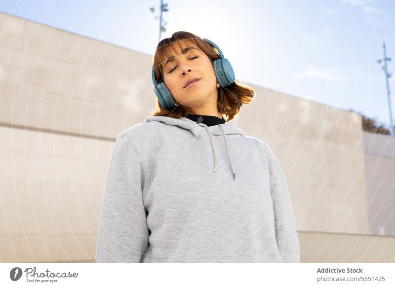 Entspannte Frau genießt Musik mit blauen Kopfhörern Erholung Zufriedenheit Genuss urban grau Kapuzenpulli Gelassenheit jung geschlossene Augen Freizeit