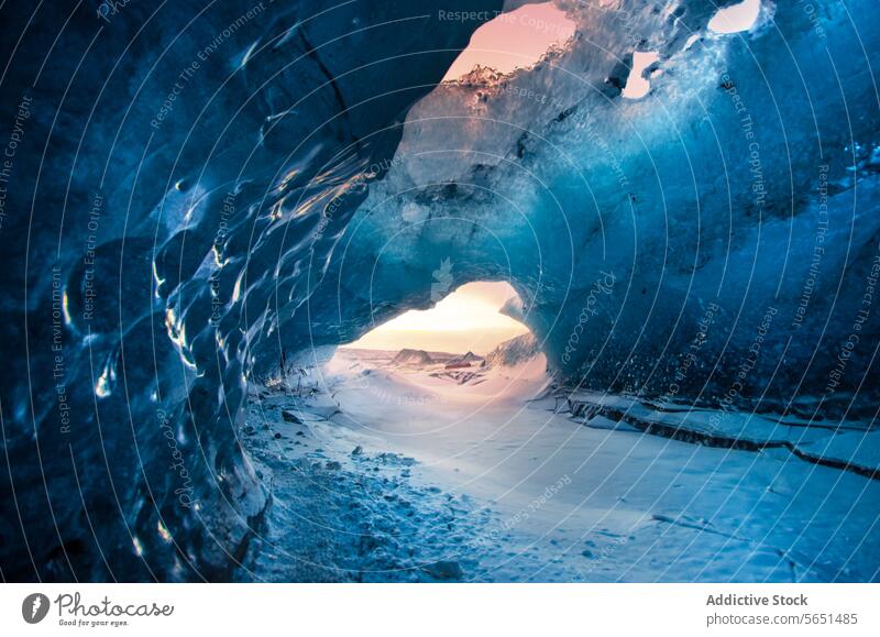 Innenansicht einer kristallblauen Eishöhle in Island mit einem durch die Öffnung sichtbaren Sonnenuntergang. Kristalle Gletscher Innenbereich Natur arktische