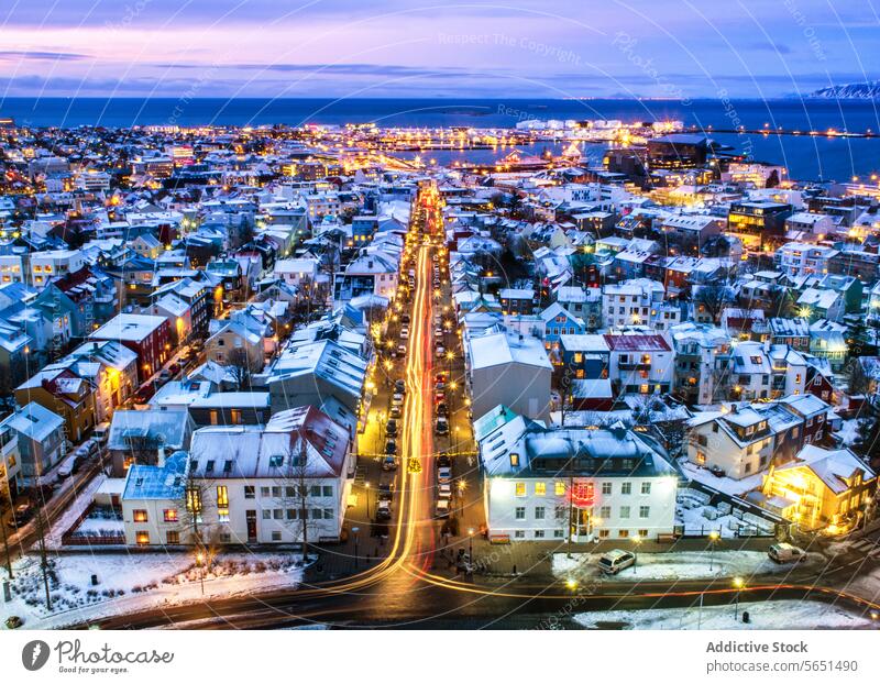 Luftaufnahme von Reykjavik in der Dämmerung mit beleuchteten Straßen, schneebedeckten Dächern und dem Meereshorizont in der Ferne Reykjavík beleuchtete Straße