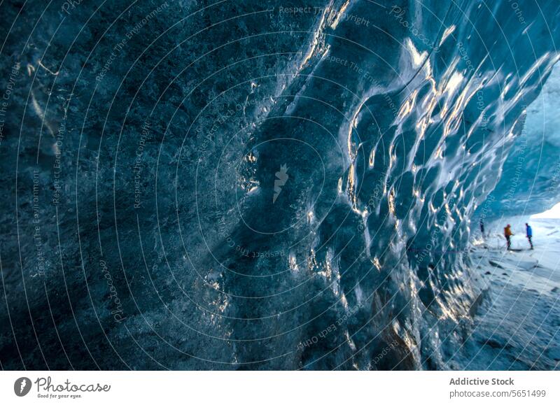 Nahaufnahme von blauem, strukturiertem Eis in einer Höhle mit Silhouetten von Menschen in der Ferne in Island Eishöhle Textur Gletscher Person Detailaufnahme
