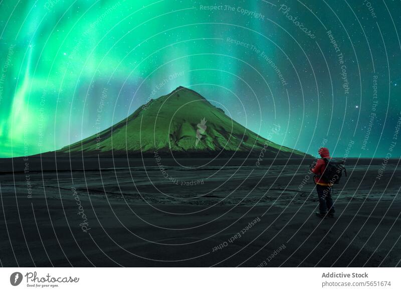 Rückenansicht einer nicht erkennbaren Person, die vor einem Vulkan unter dem pulsierenden Polarlicht in Island steht Nordlicht Beobachter Figur Silhouette Nacht