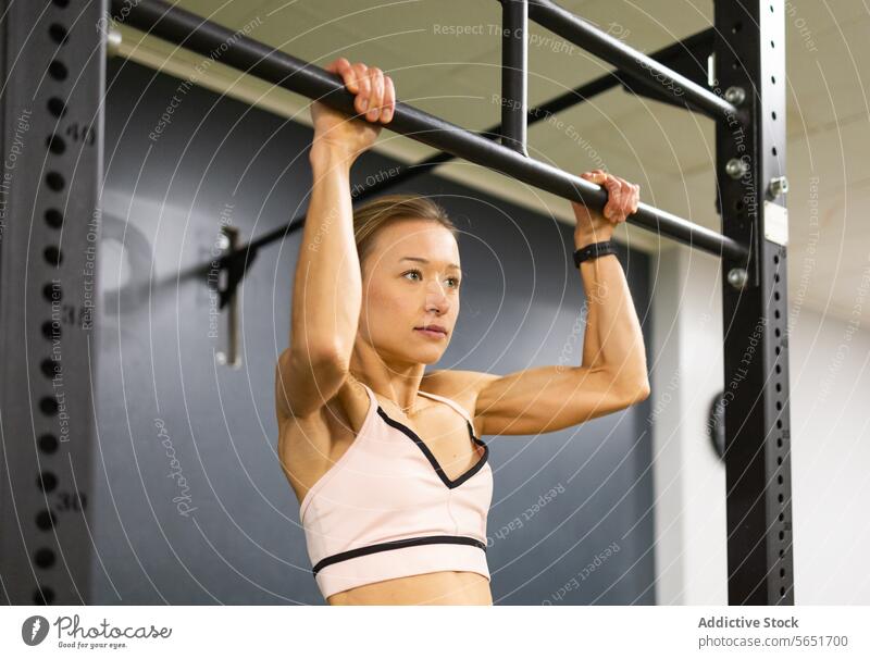 Entschlossene Frau bei einer Klimmzugübung im Fitnessstudio Übung Stärke Ausdauer Training Athlet Gesundheit Sport aktiv Tatkraft modern im Innenbereich Bar