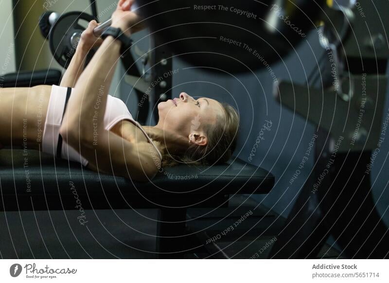 Entschlossene Frau beim Bankdrücken in einem Fitnesscenter Übung Fitnessstudio Training Stärke Gesundheit Sport sportlich Tatkraft Gewichtheben Curl-Hantel