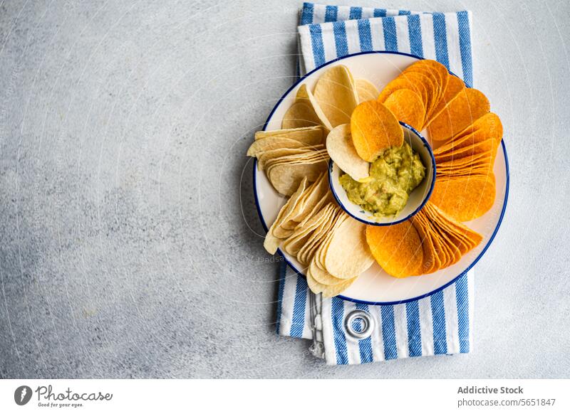 Gemischte Chips mit Guacamole im Betonhintergrund Kartoffelchips Paprika Käse Avocado Saucen Snack Teller Schalen & Schüsseln gestreift Serviette Amuse-Gueule