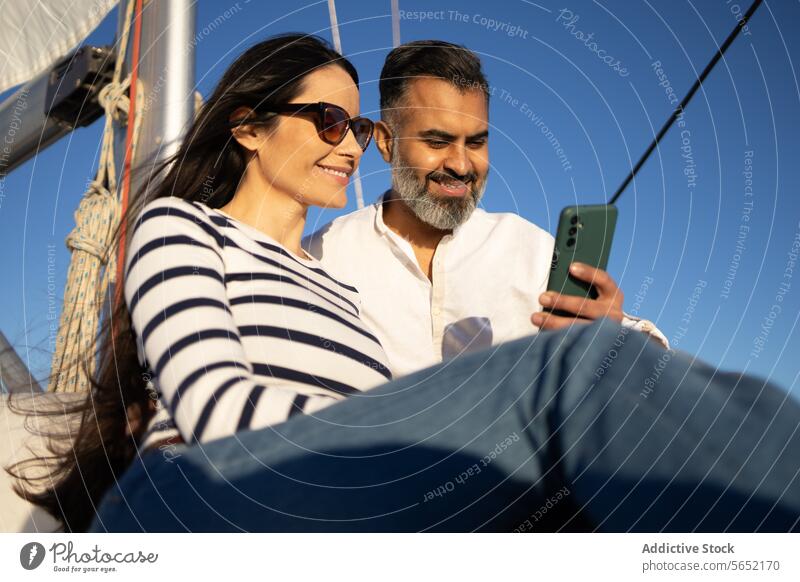 Lächelndes Paar surft auf dem Smartphone, während es auf einer Jacht sitzt benutzend Browsen Surfen Mobile Gerät Telefon Urlaub Glück reisen Funktelefon
