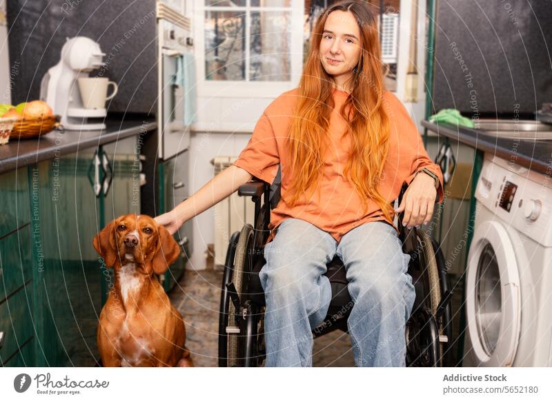 Junge Frau im Rollstuhl mit treuem Hund in der Küche Haustier heimwärts Zugänglichkeit Gesellschaft im Innenbereich gemütlich Behinderung Vorrichtung