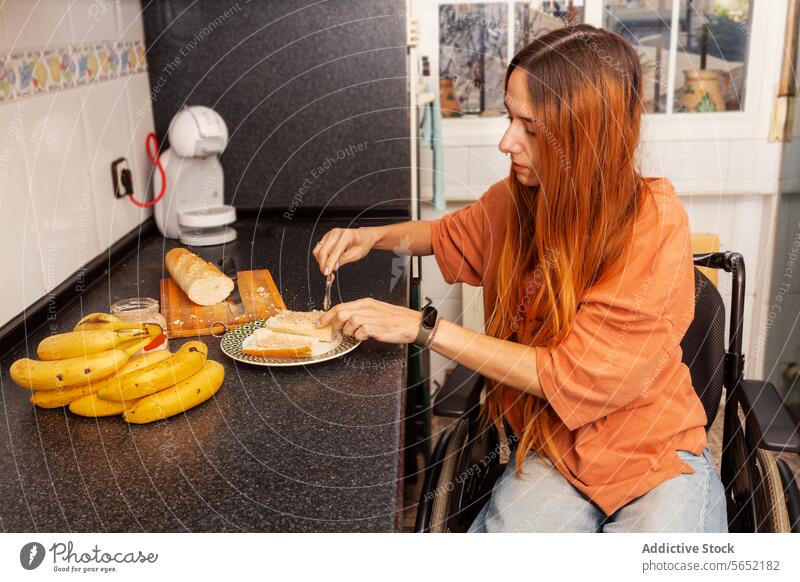 Frau im Rollstuhl bei der Zubereitung einer Mahlzeit in der Küche Selbstständigkeit Essensvorbereitung Schneiden Brot Belegtes Brot heimwärts Gerät