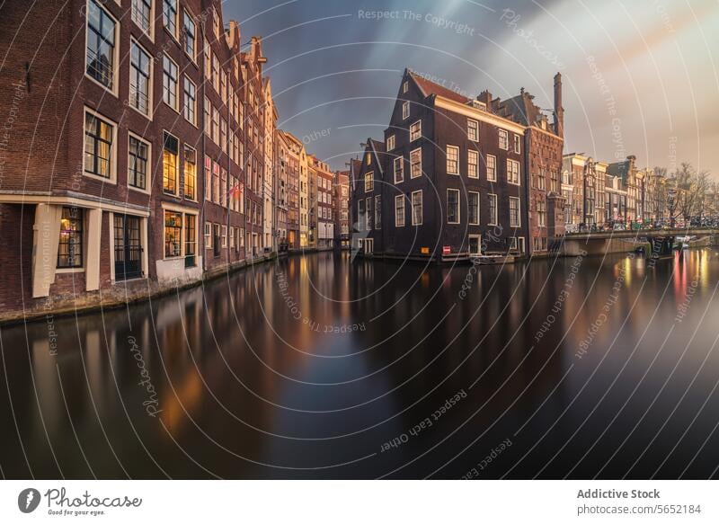 Der Sonnenuntergang wirft ein warmes Licht auf die ruhigen Amsterdamer Grachten, in denen sich die historischen niederländischen Gebäude im Wasser spiegeln