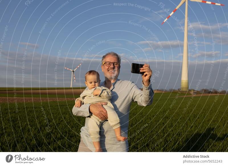 Glücklicher Großvater macht Selfie mit Enkel im Windpark Smartphone Windmühle Lächeln Natur niedlich Zusammensein Liebe futuristisch regenerativ Energie