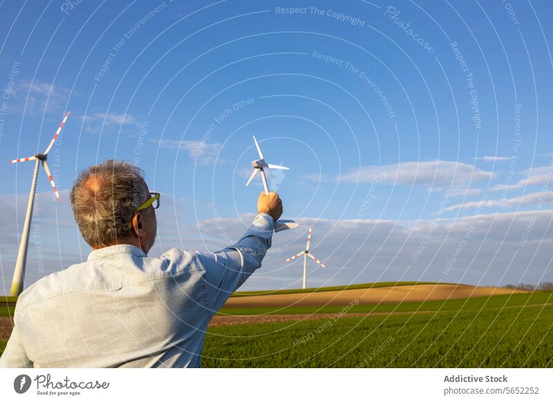 Anonymer Mann, der ein Windradmodell auf einem Feld vor blauem Hintergrund hält Windmühle Model Blauer Himmel Innovation futuristisch regenerativ Energie