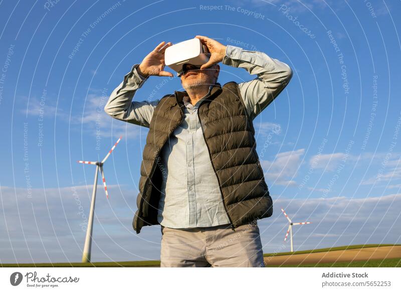 Älterer Mann mit VR-Brille vor Windrad und blauem Himmel vr-kopfhörer Windmühle Apparatur Senior Innovation futuristisch stehen älter regenerativ Energie