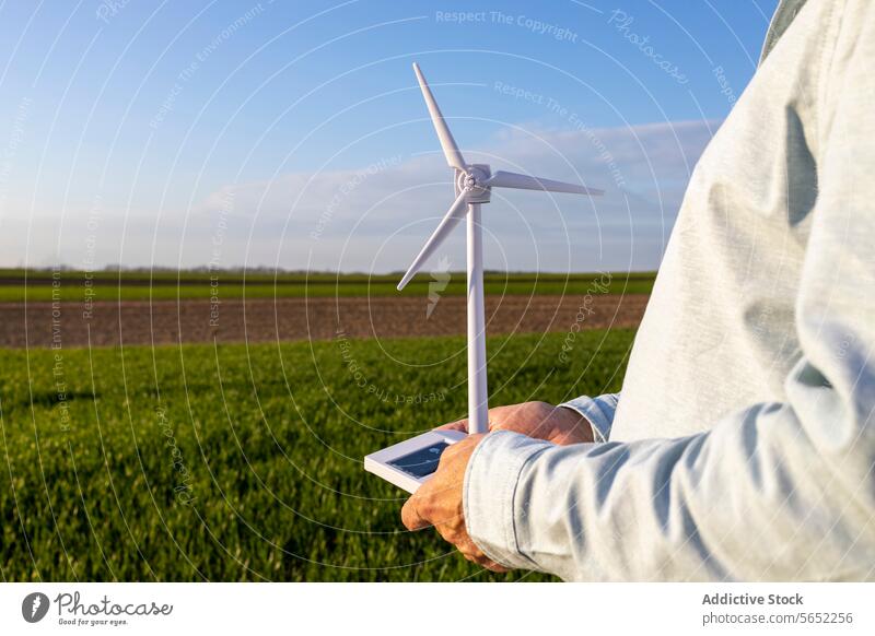 Mann hält Modell einer Windkraftanlage auf einem landwirtschaftlichen Feld vor blauem Himmel Windmühle Blauer Himmel Innovation futuristisch stehen regenerativ