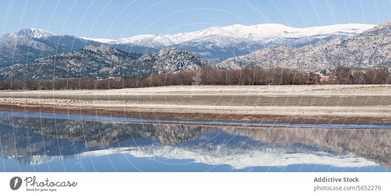 Ein Panoramablick auf einen ruhigen See mit schneebedeckten Bergen im Hintergrund und einer klaren Spiegelung im Wasser Berge u. Gebirge Schnee