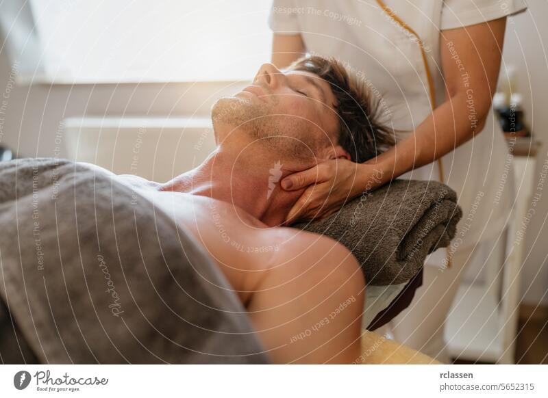 Therapeutin gibt einem männlichen Kunden in einem hellen Wellnessbereich eine Nackenmassage Physiotherapeutin Hotel Massageöle asiatisch Erholung
