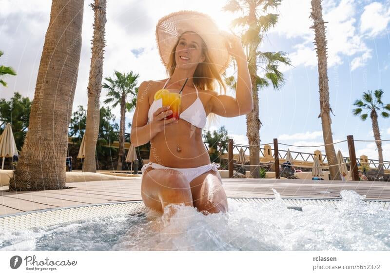Frau in weißem Bikini und Strohhut genießt ein Getränk in einem Whirlpool, mit Palmen um ein karibisches Inselhotel Hotel Pool trinken Cocktail Spaß Resort