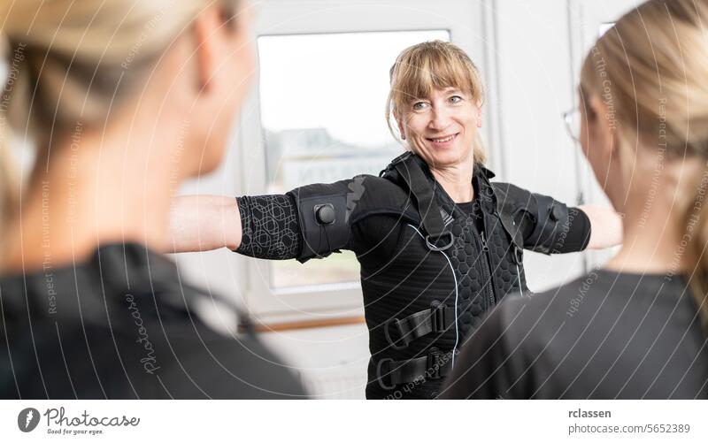 Eine Frau wird von einem Ausbilder in einem modernen EMS-Studio bei der Anprobe eines EMS-Trainingsanzugs unterstützt. passend Elektro Anregung neuromuskulär