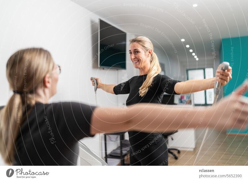 Fitness-Kunde lächelnd, während er die Griffe der Körperanalysewaage Inbody Test hält und die Arme in Richtung des Trainers in einem EMS - Studio ausstreckt.
