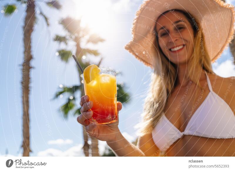 Frau in weißem Bikini und Strohhut bietet einen tropischen Cocktail, sonnigen Himmel mit Palmen. Party und Sommerurlaub Konzeptbild auf einer karibischen Insel.