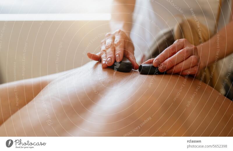 Nahaufnahme einer Hot-Stone-Massage auf dem Rücken einer Person mit den Händen des Therapeuten. Wellness Hotel Konzept Bild asiatisch Schönheitssalon Druckpunkt