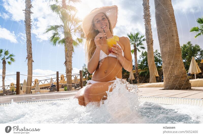 Frau im Bikini mit Hut, trinkt Cocktail im Whirlpool, Palmen und Resort Hintergrund im Hotel auf einer Insel Fuerteventura Pool trinken Spaß jubelt sonnig