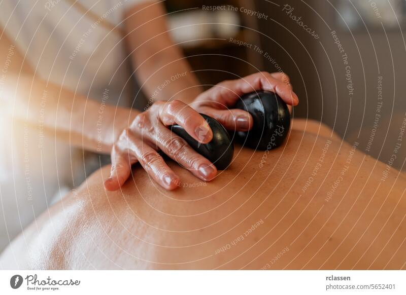 Massagetherapeutin, die während einer Spa-Behandlung heiße Steine auf den Rücken des Kunden legt. Wellness Hotel Konzept Bild Physiotherapeutin Massageöle