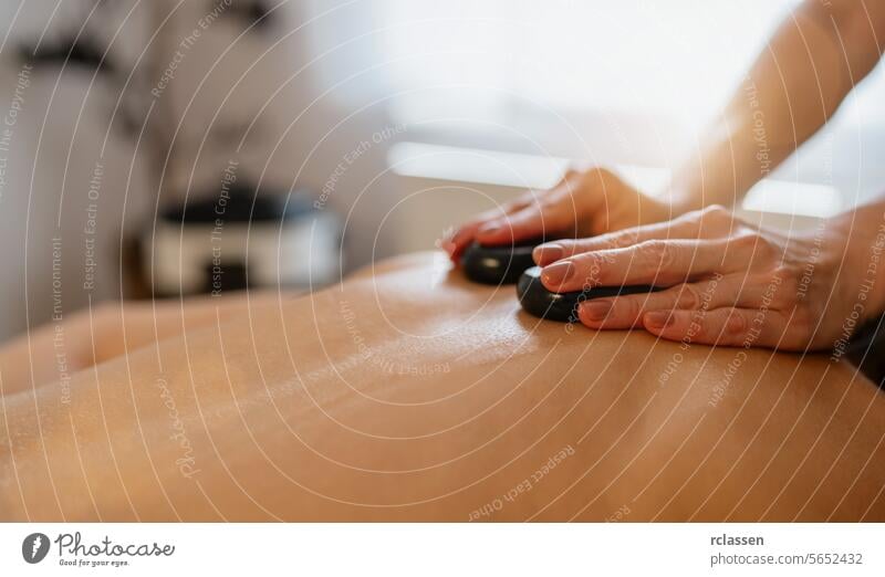Nahaufnahme einer Hot-Stone-Massage auf dem Rücken einer Person mit den Händen des Therapeuten. Schönheitssalon Wellness Hotel Konzeptbild asiatisch Druckpunkt
