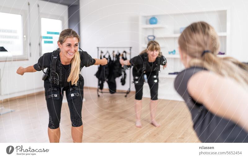 Zwei Frauen in EMS-Trainingsanzügen machen Gleichgewichtsübungen vor einem Trainer in einem Fitnessstudio Elektro Anregung neuromuskulär elektrisch muskulös