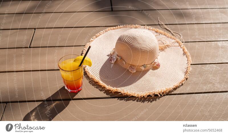 Sommercocktail mit Strohhut auf einer Holzterrasse, die Entspannung und Urlaubsstimmung symbolisiert Party Karibik-Insel-Hotel Cocktail Obstbeilage sonnig