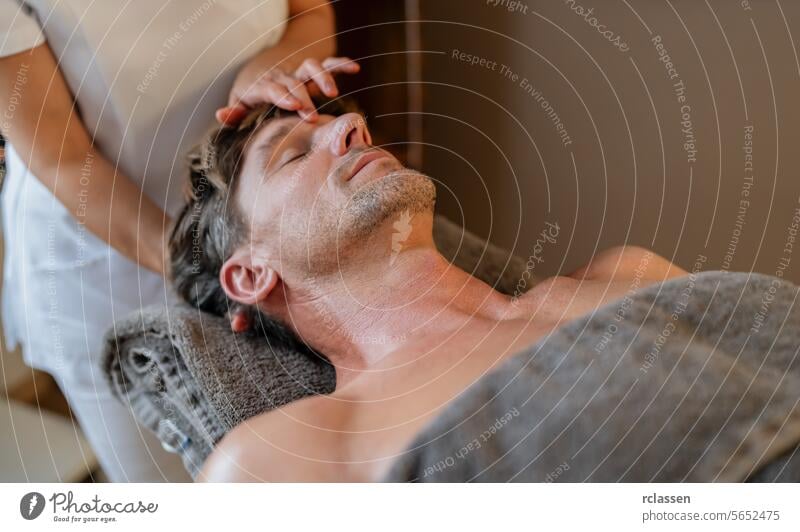 Mann entspannt sich bei einer Kopfmassage in einem Spa mit den Händen des Therapeuten auf der Stirn männlicher Patient Wellness Stressabbau Körperpflege