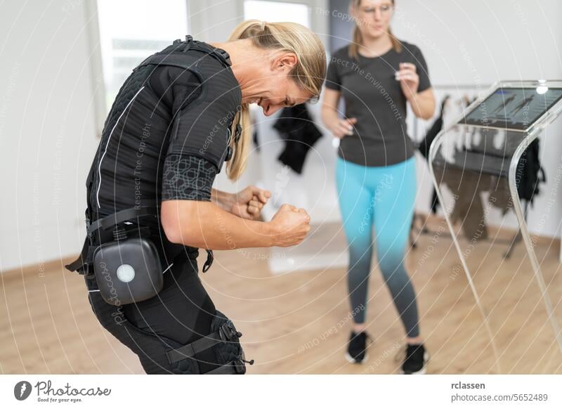 Frau im EMS-Anzug führt Übungen unter Anleitung eines Trainers in einem Fitnessstudio durch Elektro Anregung neuromuskulär elektrisch muskulös Frau beim Sport