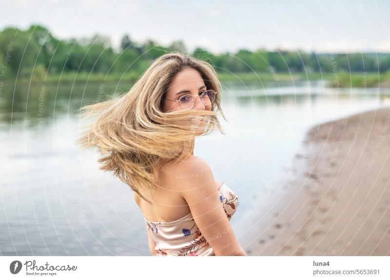 glückliche junge Frau mit wehenden Haaren steht am Fluss frau haare zerzaust lachen wind sinnlich windig anmutig hübsch single fröhlich porträt attraktiv