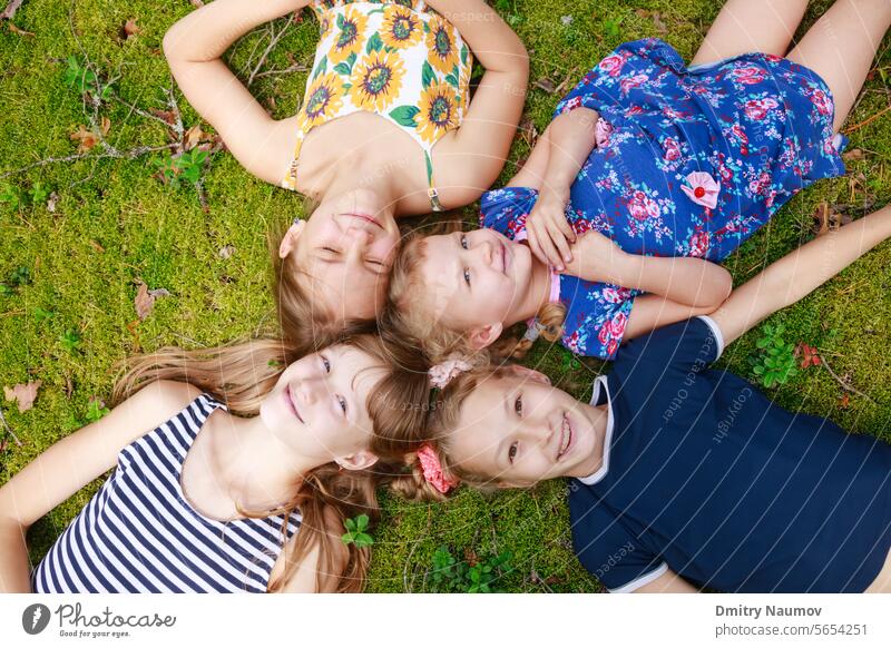 Mädchen unterschiedlichen Alters liegen zusammen auf einem Moos in einem Sommerwald und genießen die Sommerferien im Freien oben Camping offen sorgenfrei heiter