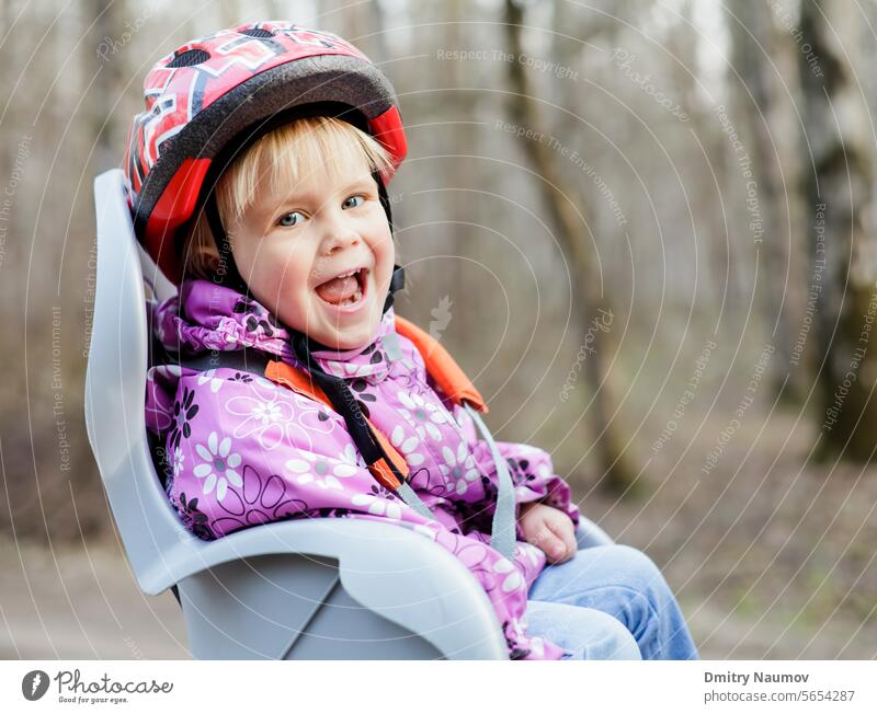 Glückliches kleines Mädchen mit Helm im Kindersitz eines Fahrrads 2 Jahre Herbst Baby Biker Radfahren Kaukasier Stuhl heiter Kindheit niedlich Zyklus