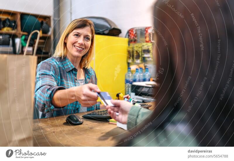 Lächelnde Verkäuferin, die die Kreditkarte eines Kunden entgegennimmt, um den Kauf abzurechnen. Konzept für den lokalen Handel Werkstatt Assistent Frau unter