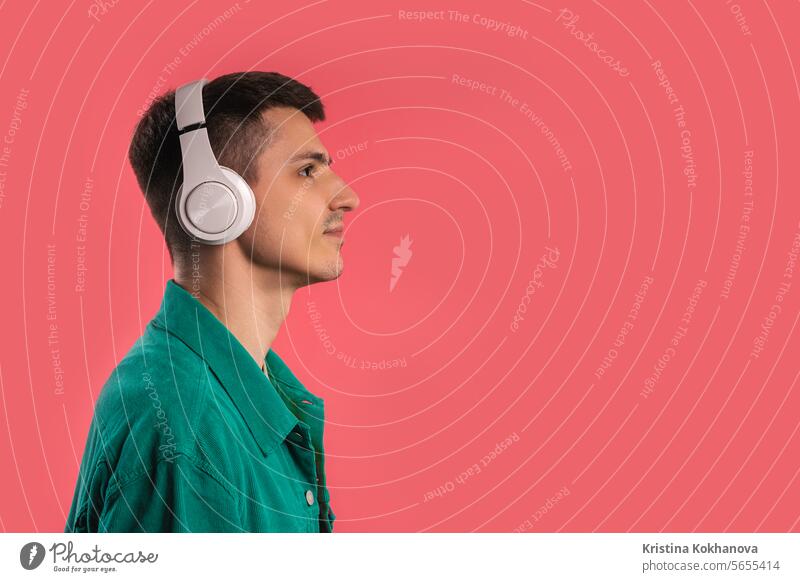 Positiver Mann hört Musik, genießt Tanz mit Kopfhörern auf rosa Studio aktiv Erwachsener schlagen lässig farbenfroh lockig Tanzen Energie schönes Lied Europäer