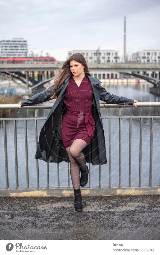 entspannte junge Frau mit schwarzem Mantel steht auf einer Brücke frau nachdenklich sinnlich verträumt sebstbewusst elegant emanzipiert träumen urban glücklich