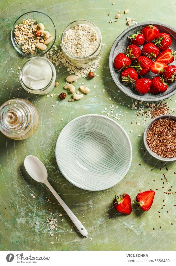 Gesundes Frühstück Schüssel Vorbereitung mit Haferflocken, Joghurt, Leinsamen, Nüsse und Erdbeeren auf grünen Tisch Hintergrund, Ansicht von oben