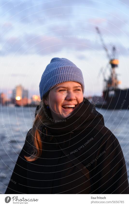 FREUDE - LACHEN - HAMBURG Frau 18-30 Jahre lachen herzig Mütze blau Hamburg Elbphilharmonie Wasser Sonnenuntergang Hafen Farbfoto Hafenstadt Außenaufnahme Elbe