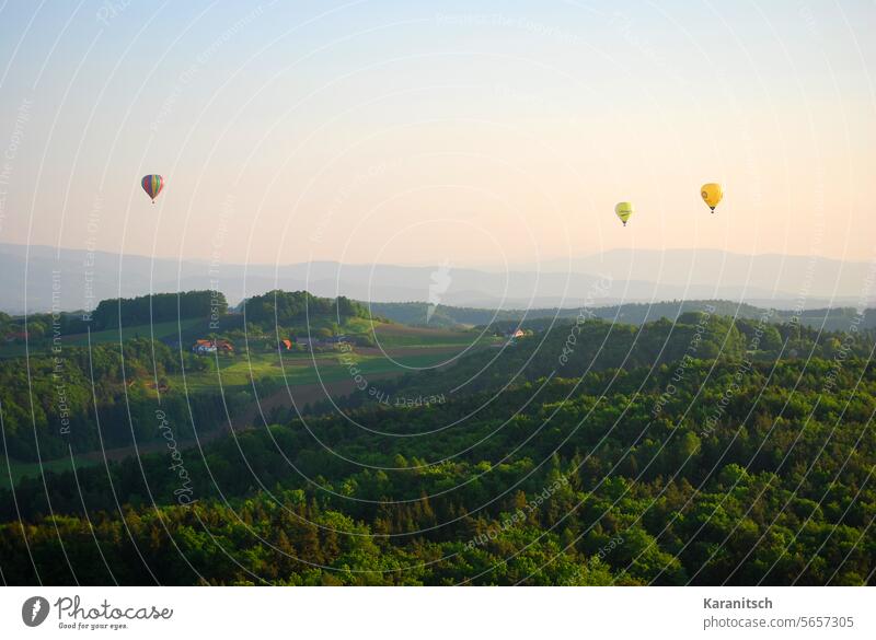 Drei Heißluft-Ballons schweben über die oststeirische Hügellandschaft. drei fahren reisen Abenteuer Landschaft hügelig Wald Wiesen Felder Morgen Morgenstimmung
