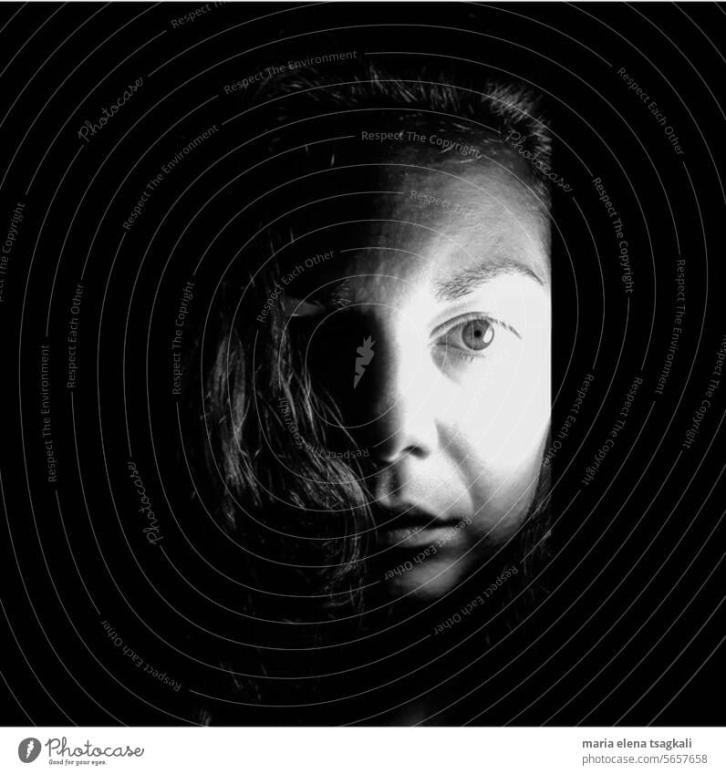 Schwarz-Weiß-Gesichtspotrait einer Frau, die direkt in die Kamera blickt, wobei der Kontrast von Licht und Schatten die ganze Atmosphäre ausmacht
