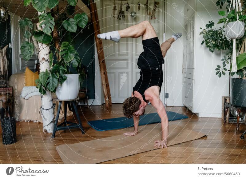 Junger Mann macht einen Handstand in einem schönen Wohnzimmer auf einer Yogamatte Personal Trainer Fitnessmatte Workout Training Gesundheit gemütlich