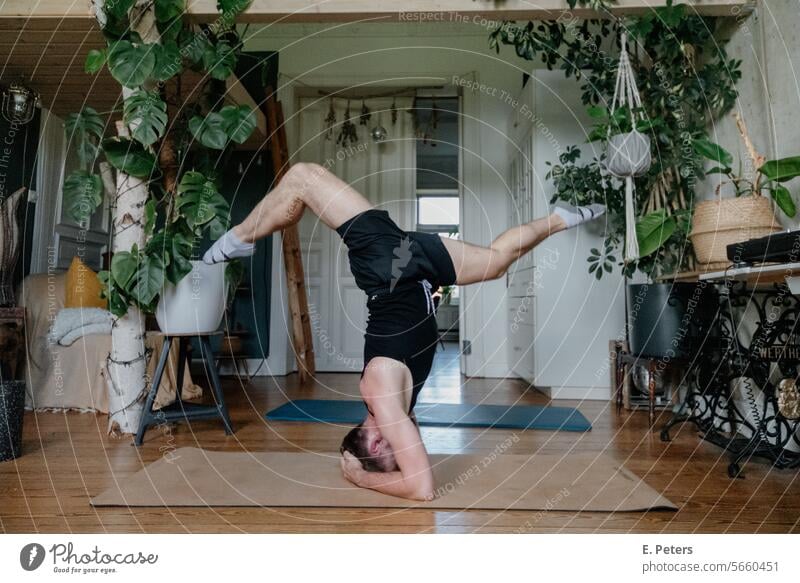 Junger Mann macht einen Handstand Spagat in einem schönen Wohnzimmer auf einer Yogamatte Personal Trainer Fitnessmatte Workout Training Gesundheit gemütlich