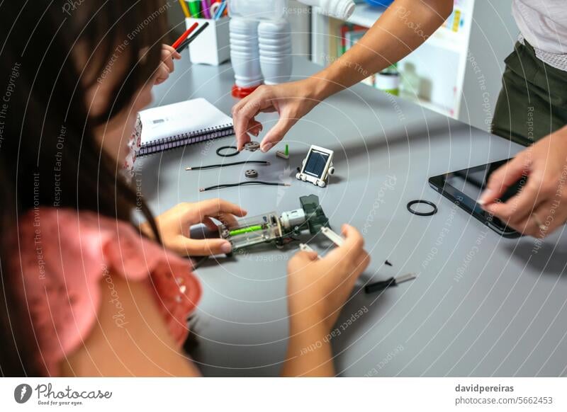 Lehrerin hilft Schülerinnen beim Zusammenbau von Maschinenteilen in einem Robotikkurs unkenntlich Frau Hilfe zu erklären. Kind versammeln elektronisch