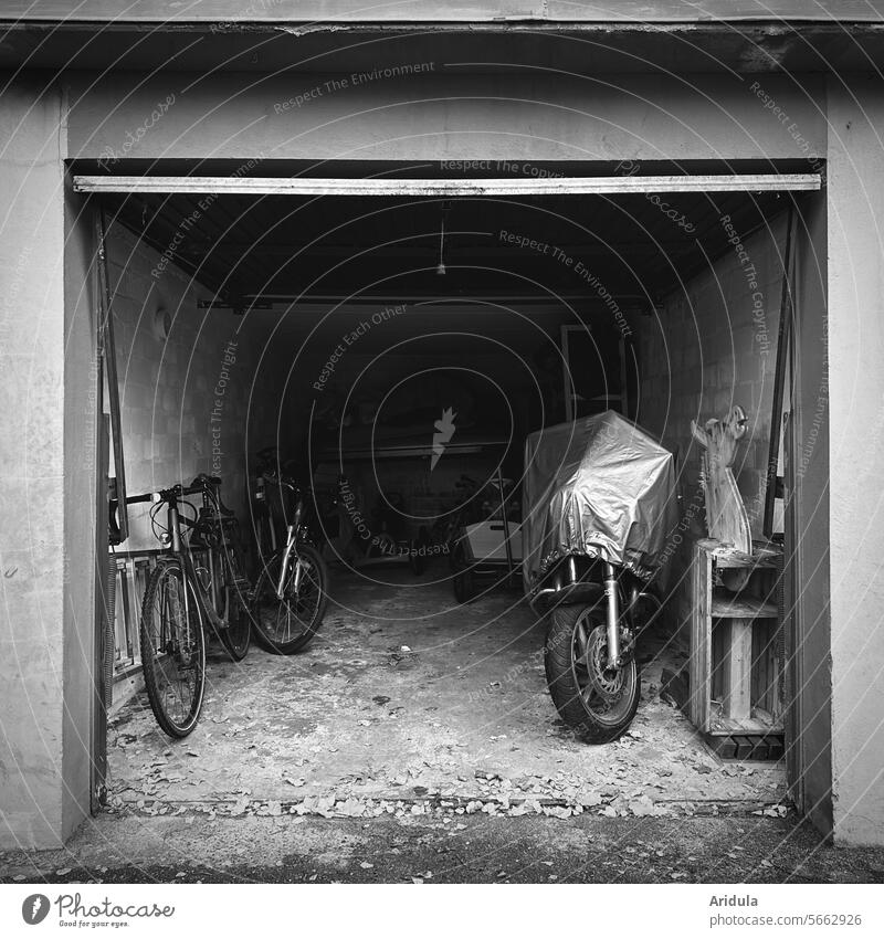 Blick in eine offene alte Garage s/w Garagentor Fahrrad Fahrräder Motorrad Abdeckung Motorradabdeckung Bollerwagen aufbewahren Tor Fahrzeug Einfahrt grau dunkel