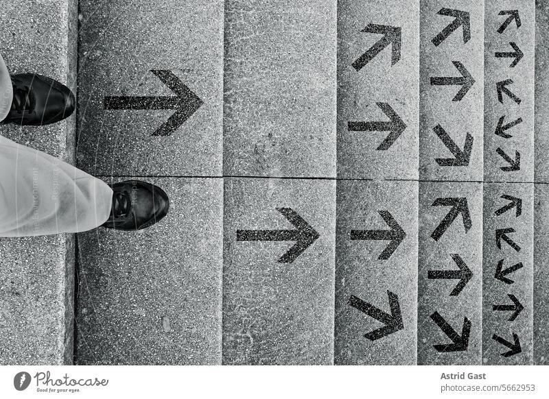 Eine Frau steht auf einer Treppe und muss entscheiden in welche Richtung sie gehen will person frau treppe stufen richung pfeile entscheidung weg hinunter