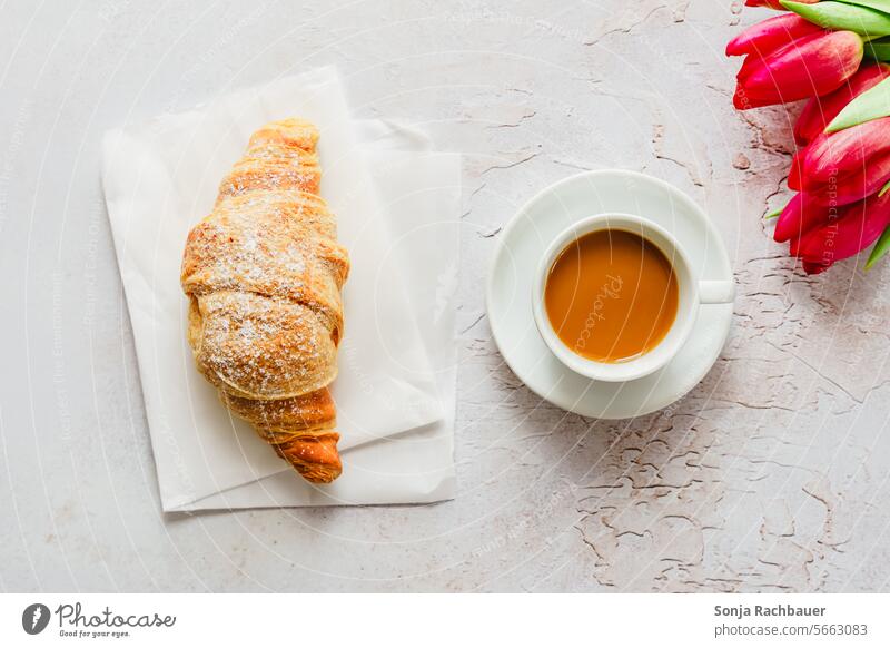 Eine Tasse Kaffee, ein Croissant und pinke Tulpen auf einem Tisch. Draufsicht. frisch Frühstück Morgen Getränk Lebensmittel rustikal grau Untertasse