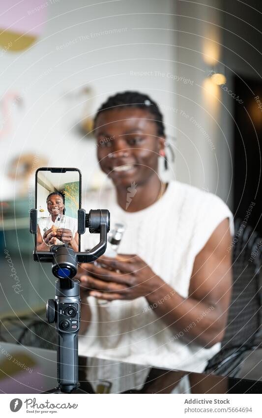 Fröhlicher schwarzer Mann nimmt ein Hautpflege-Tutorial mit einem Smartphone und Gimbal vor einem modernen Innenhintergrund auf Aufnahme Kardangelenk heiter