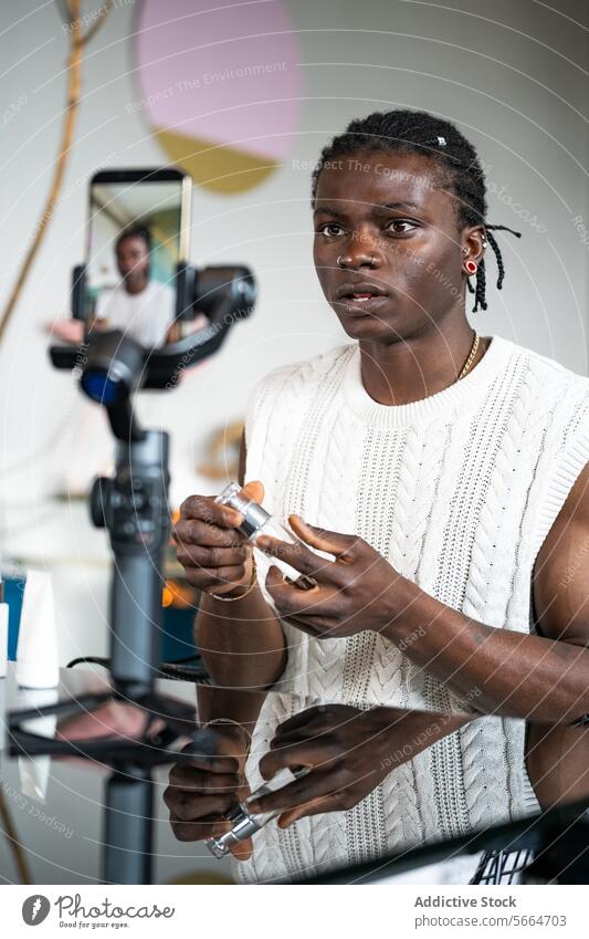 Ein fokussierter schwarzer Mann in einem weißen Pullover erklärt Produktmerkmale, während er ein Hautpflegetutorial filmt Tutorial Dreharbeit Produkterläuterung