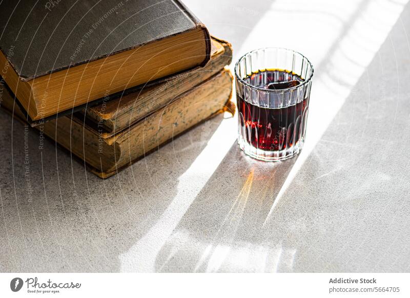 Kirschlikör in einem klaren Glas neben einem Stapel alter Bücher auf einer sonnenbeschienenen Fläche Kirsche Likör Buch altehrwürdig Sonnenlicht Schatten
