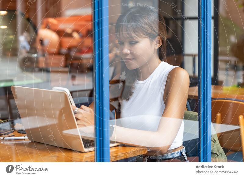Eine asiatische Frau konzentriert sich auf ihr Smartphone und ihr Tablet in einem Café während einer Fernarbeit in Chiang Mai, Thailand fokussiert Tablette